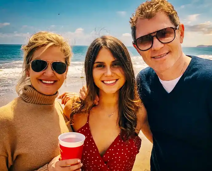 Kate Connelly and Bobby Flay, together with their daughter Sophie Flay, posing with embracing shoulders of each other against ocean waves