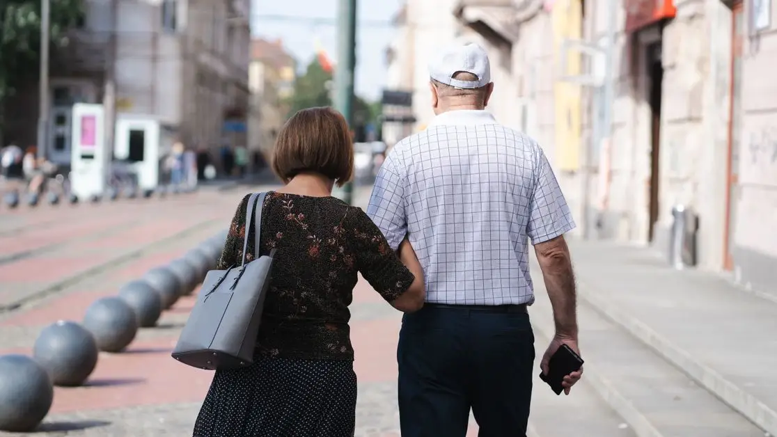 Senior couple walking arm-in-arm on a sunny urban street, capturing a moment of togetherness